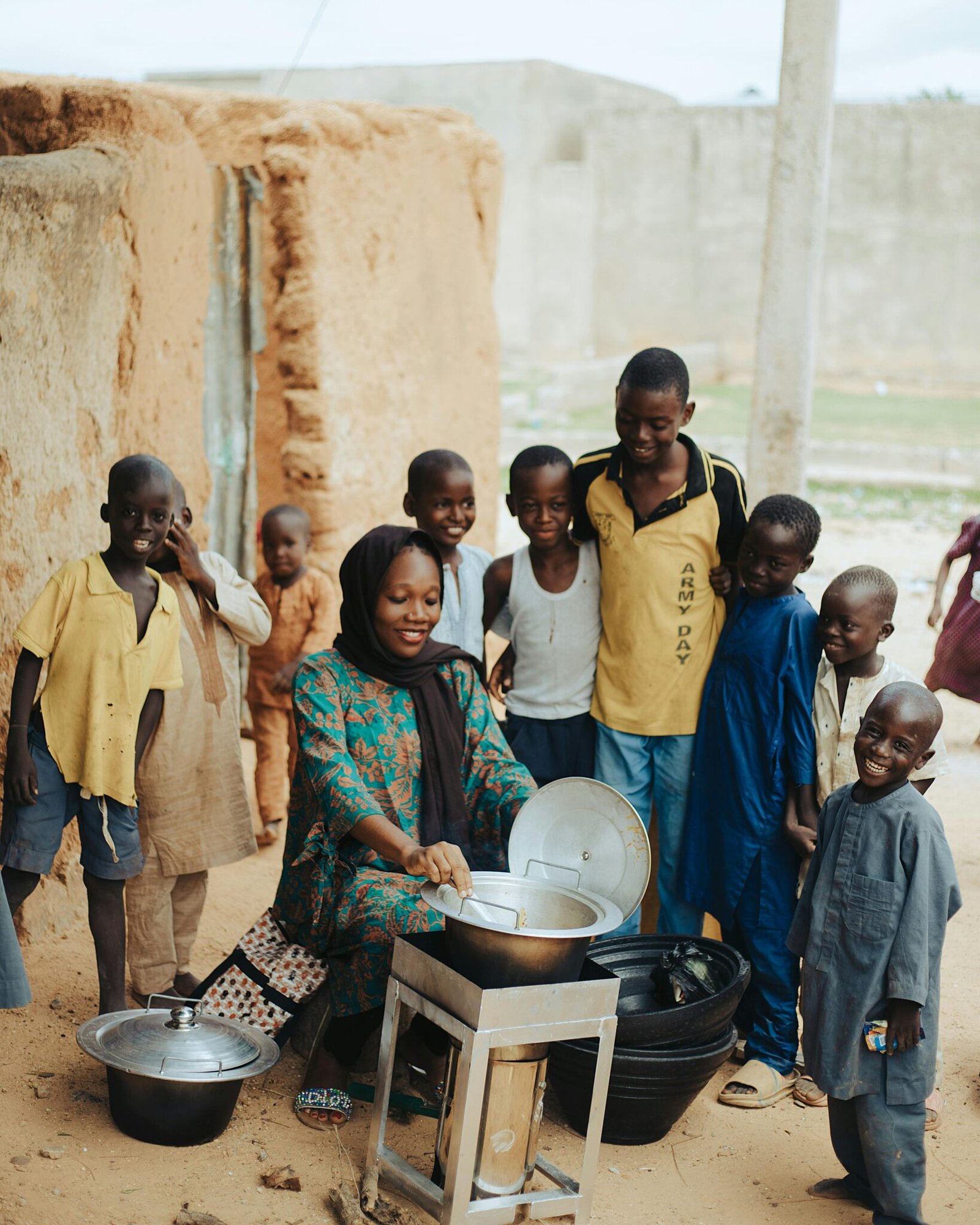 A woman cooking while surrounded by children outdoors in a rural setting, showcasing community life.
